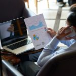 Vedere peste umăr a unui bărbat care efectuează multitasking și revizuiește documente financiare și are o conversație telefonică